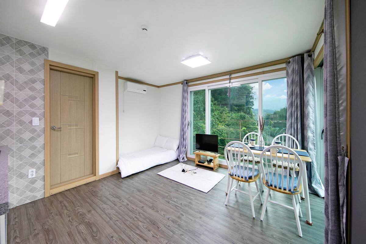 A modern room with a wooden floor, a white sofa, a TV on a wooden stand, and a dining area with white chairs.