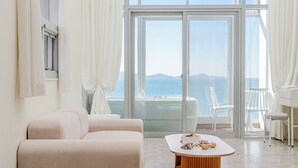Ein modernes Wohnzimmer mit Sofa, Couchtisch und Meerblick durch große Glasfenster.
