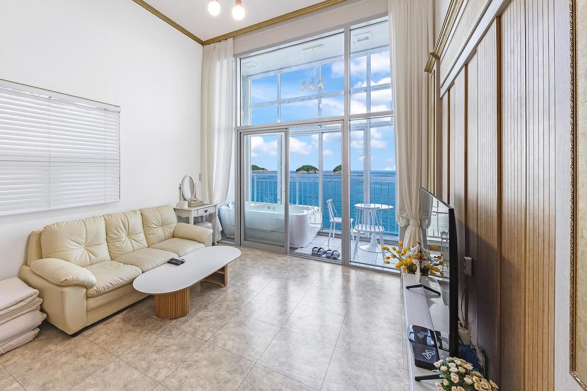 Un salón amplio con un sofá color beige, una mesa de centro y vistas al mar a través de amplios ventanales.