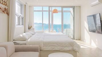 A modern hotel room with a large bed, a seating area, and a view of the sea.