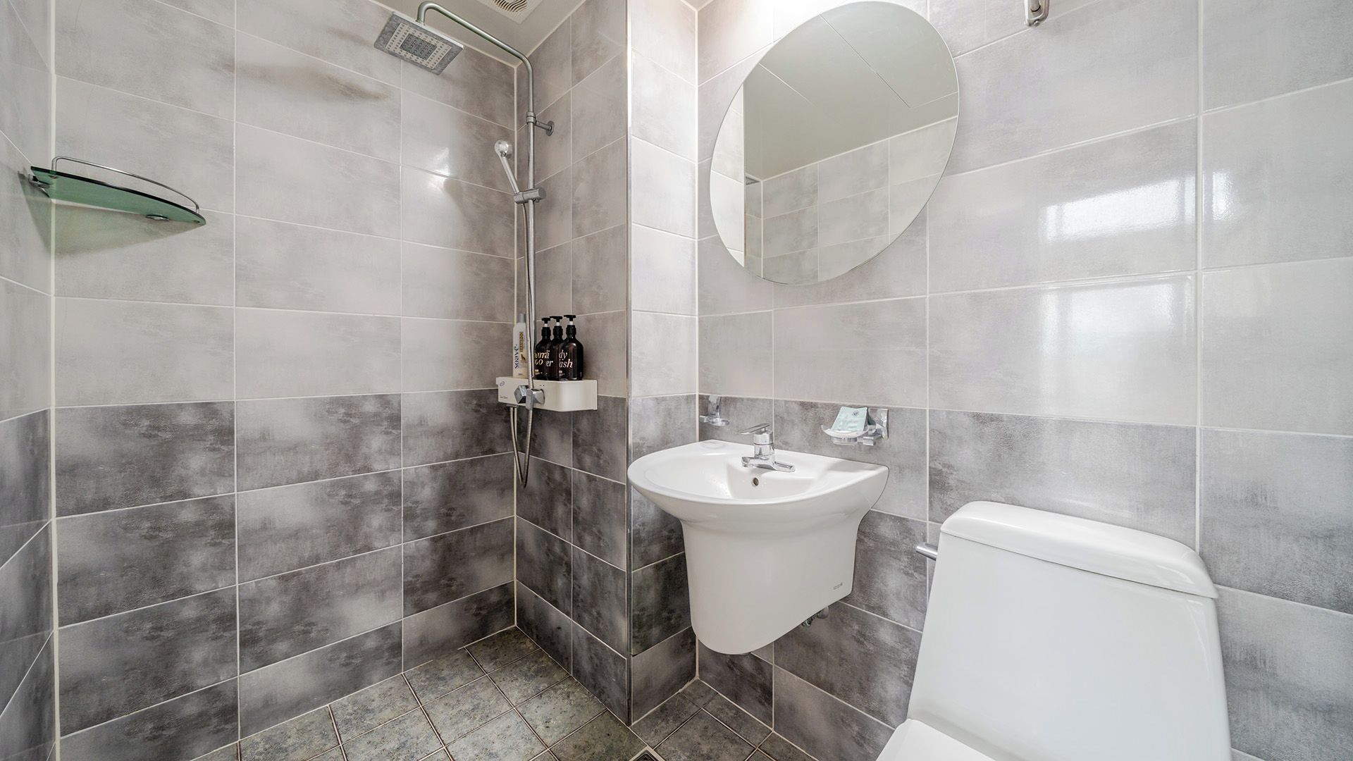 Un bagno con doccia, lavandino, WC e ripiano in vetro.