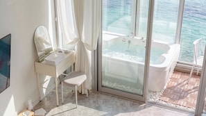 A modern bathroom with a glass-enclosed jacuzzi, a vanity with a mirror, and a view of the sea. - Yeosu Nukim Pension (Yeosu)