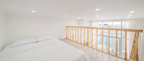 A bedroom with a large bed, a wooden railing, and a view of the sea.