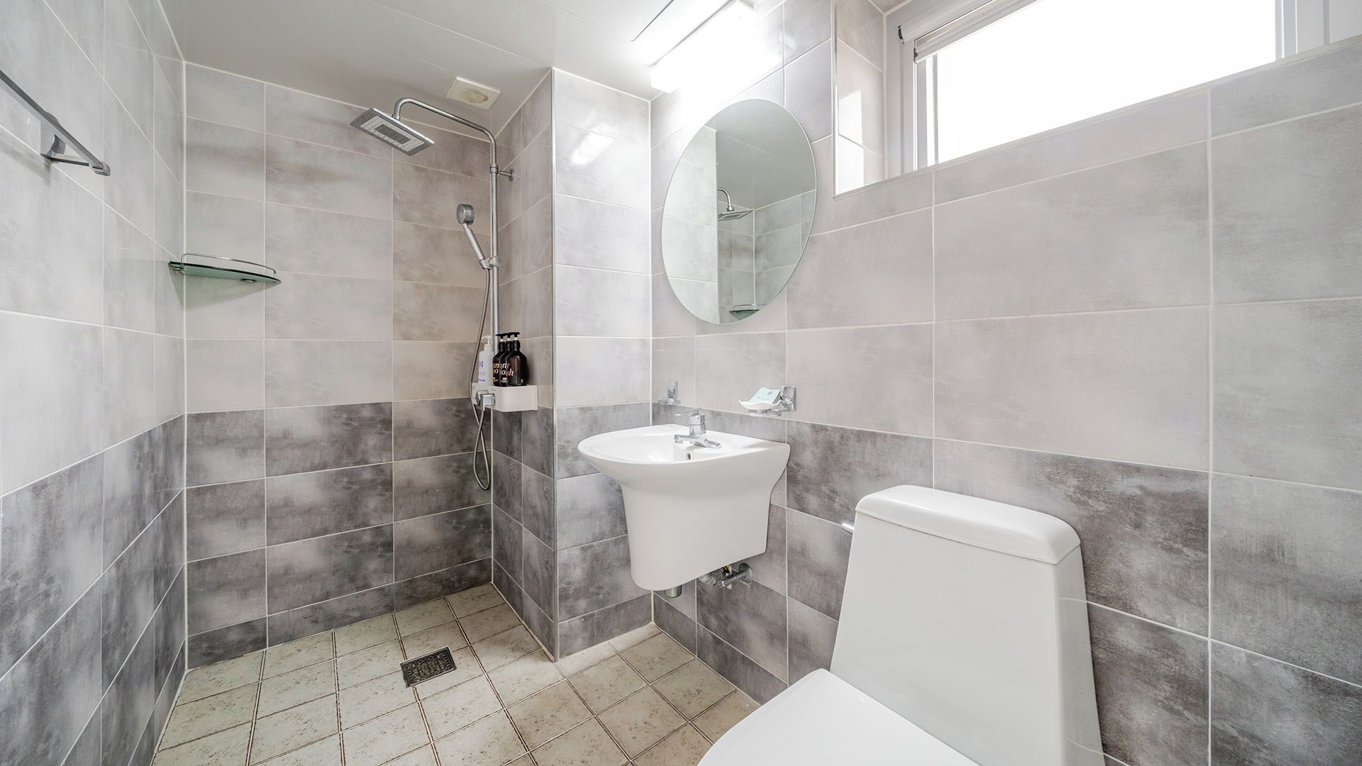 Et moderne badeværelse med bruser, vask, toilet og spejl.