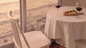 A table with two wine glasses, a cheese board, and a chair by a window overlooking a beach. - Yeosu Nukim Pension (Yeosu)