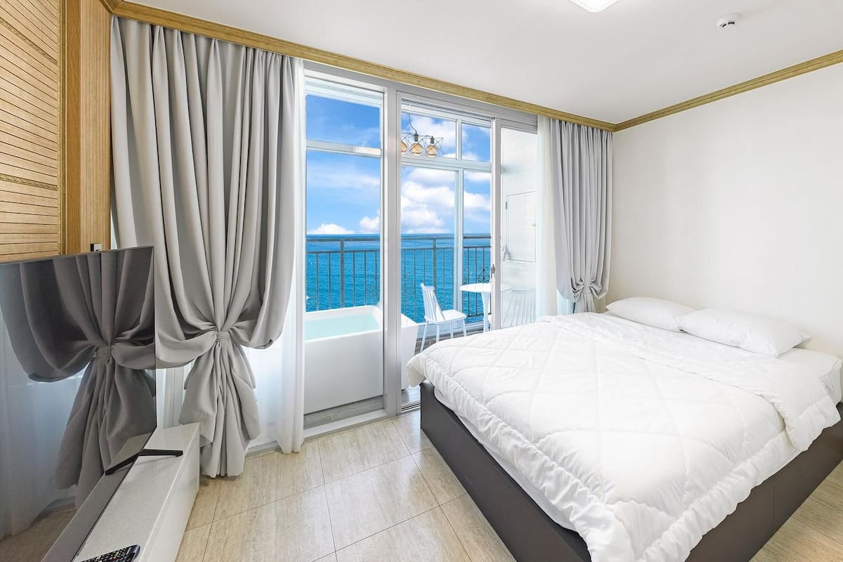 Habitación de hotel con cama, televisor y balcón con vista al mar.