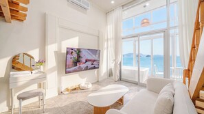 A modern living room with a large TV, a sofa, a dining table, and a view of the sea. - Yeosu Nukim Pension (Yeosu)