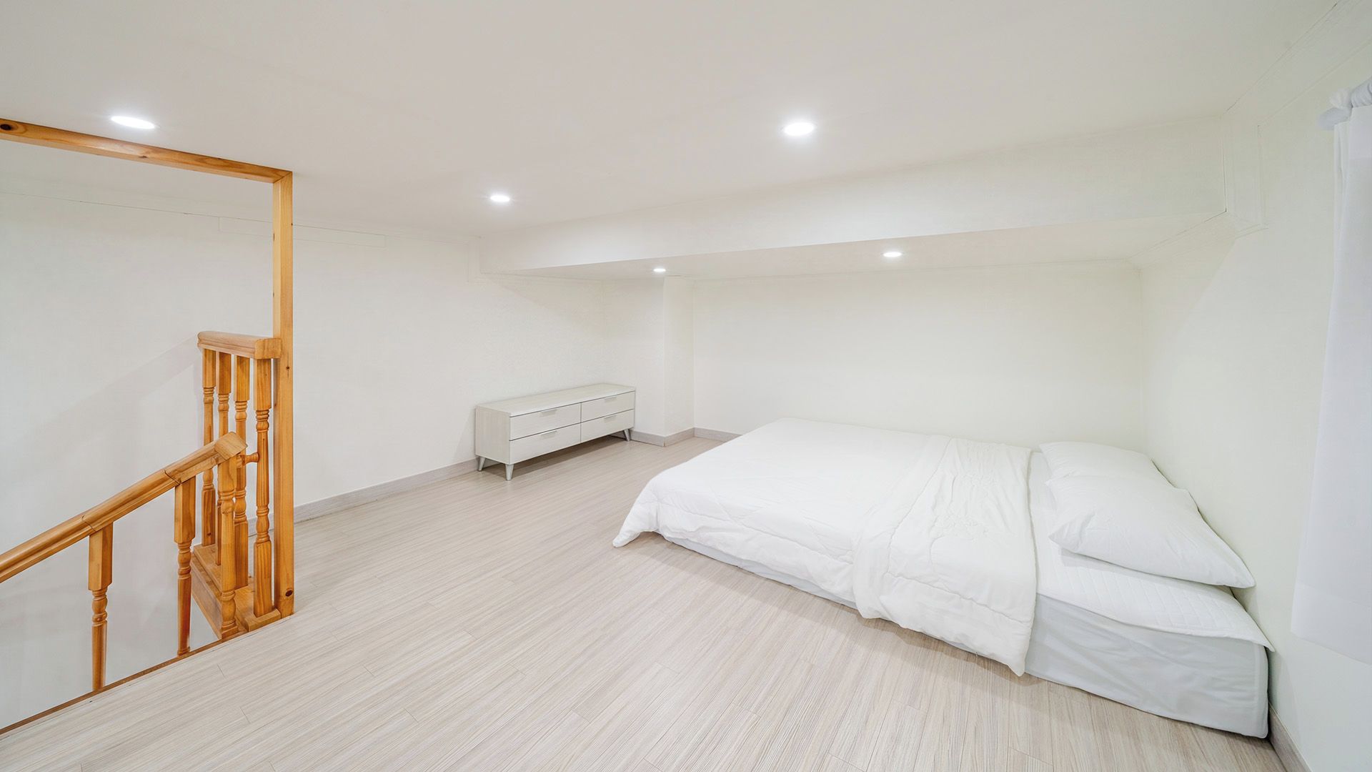 A bedroom with a bed, a dresser, and a wooden staircase.
