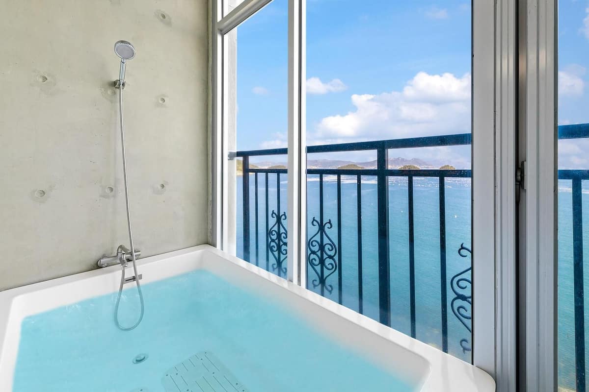 Un baño con bañera y ventana con vistas panorámicas al océano.