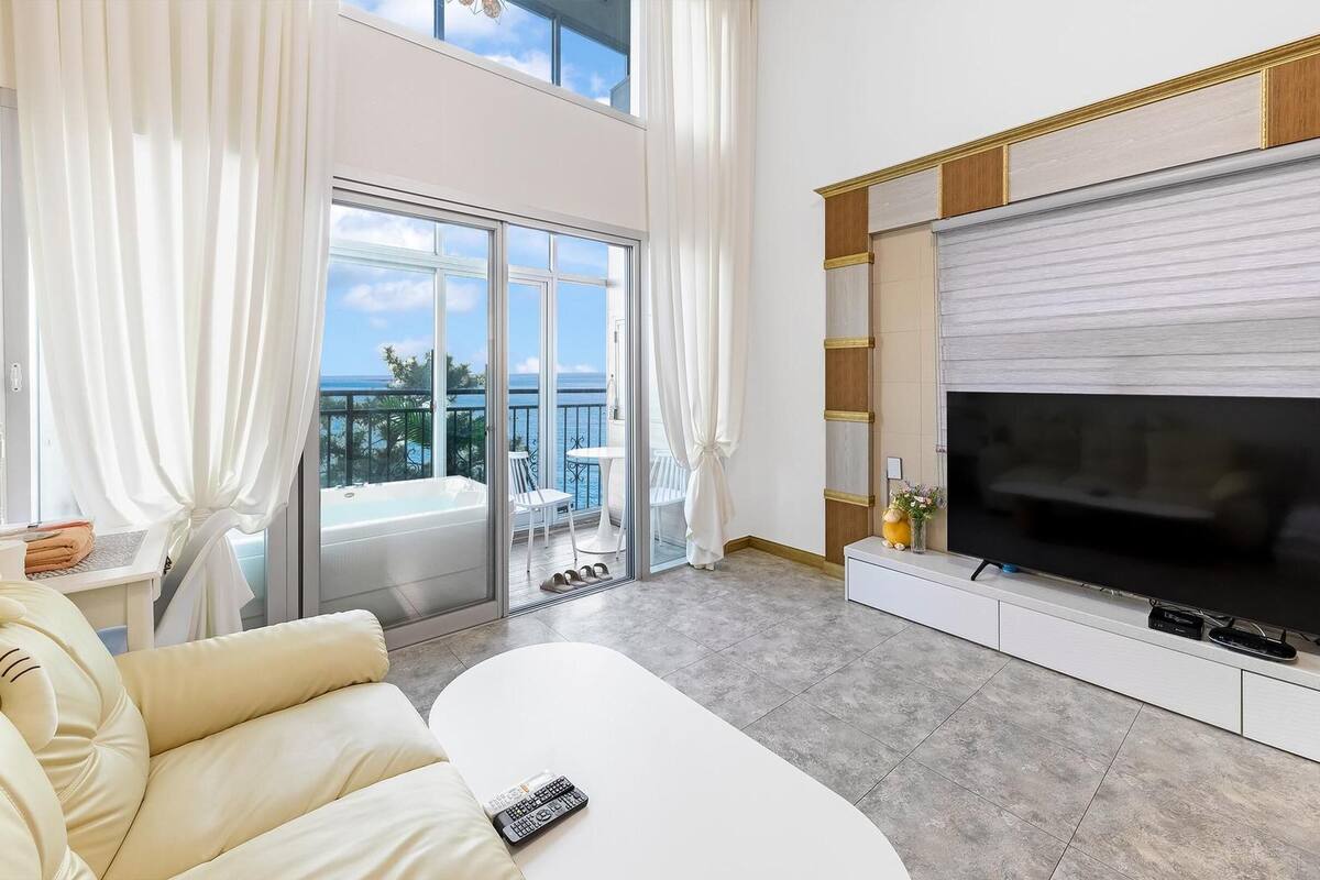 Una sala de estar moderna con un televisor de pantalla plana grande, un sofá y un balcón con vistas al mar.