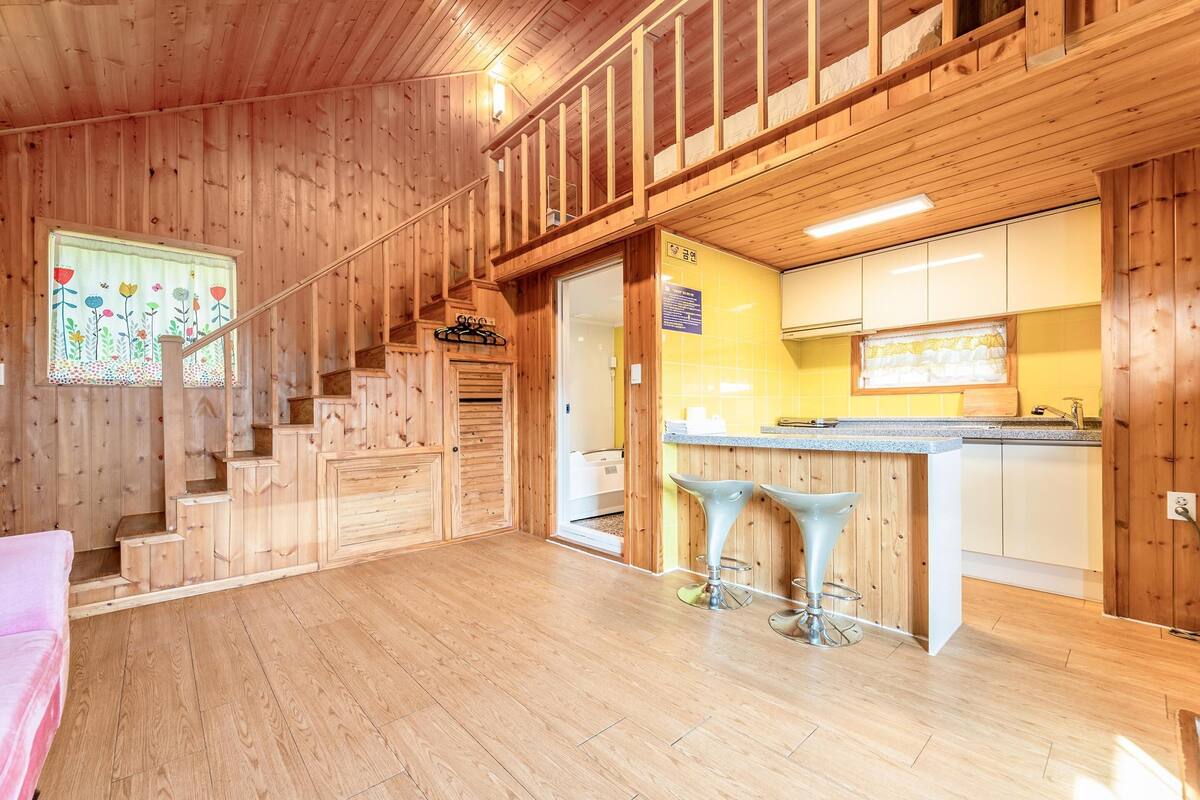 Un interior de madera con una escalera, una zona de cocina con barra y un comedor.