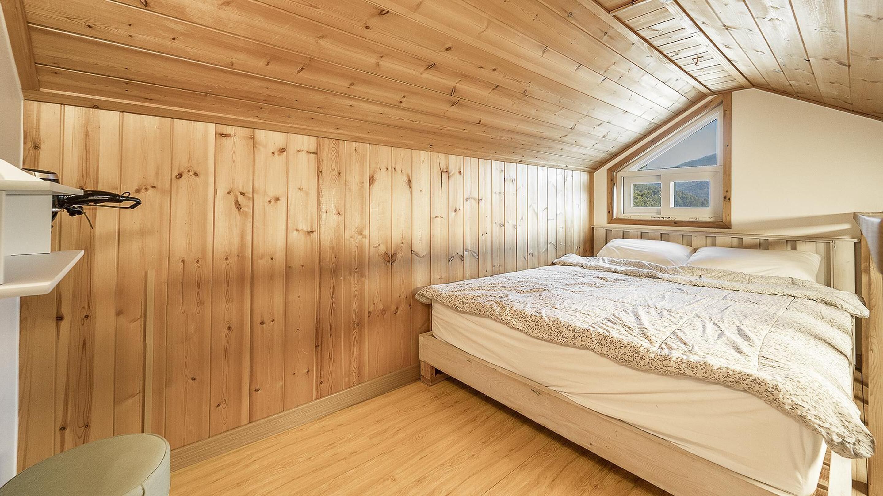 A wooden-paneled room with a bed, a window, and a small table.