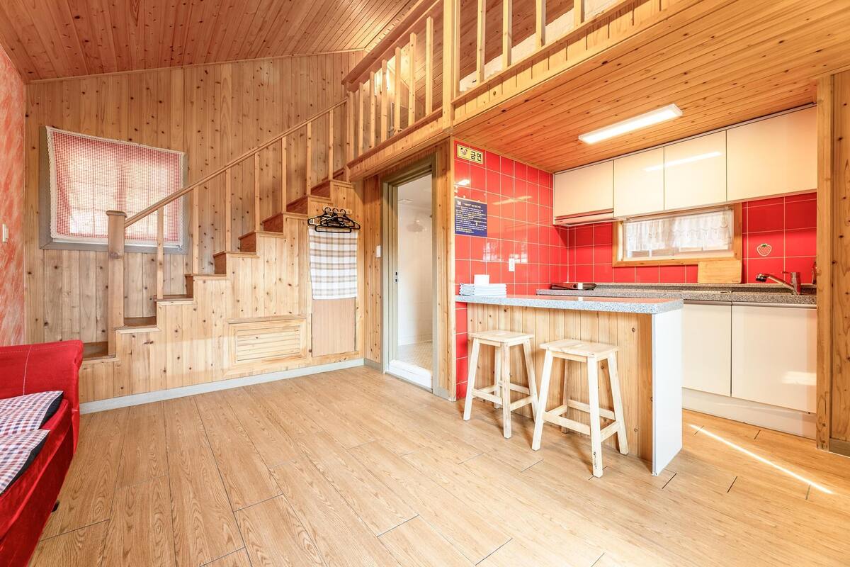 Un interior de madera con una zona de cocina, una escalera y un salpicadero de azulejos rojos y blancos.