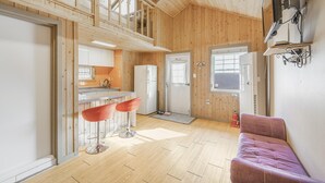 Une cuisine compacte équipée d’un réfrigérateur, d’un évier et de tabourets de bar. Un canapé violet se trouve dans l’espace salon, près d’une fenêtre.