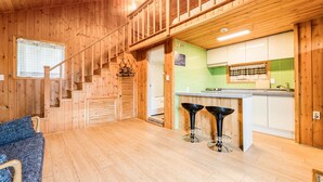 Un interior de madera con una escalera, una zona de cocina con salpicadero verde y dos taburetes negros.