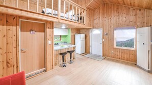 Une cabane en bois comprenant une cuisine, un coin repas avec deux tabourets, un balcon et une fenêtre donnant sur un paysage agréable.
