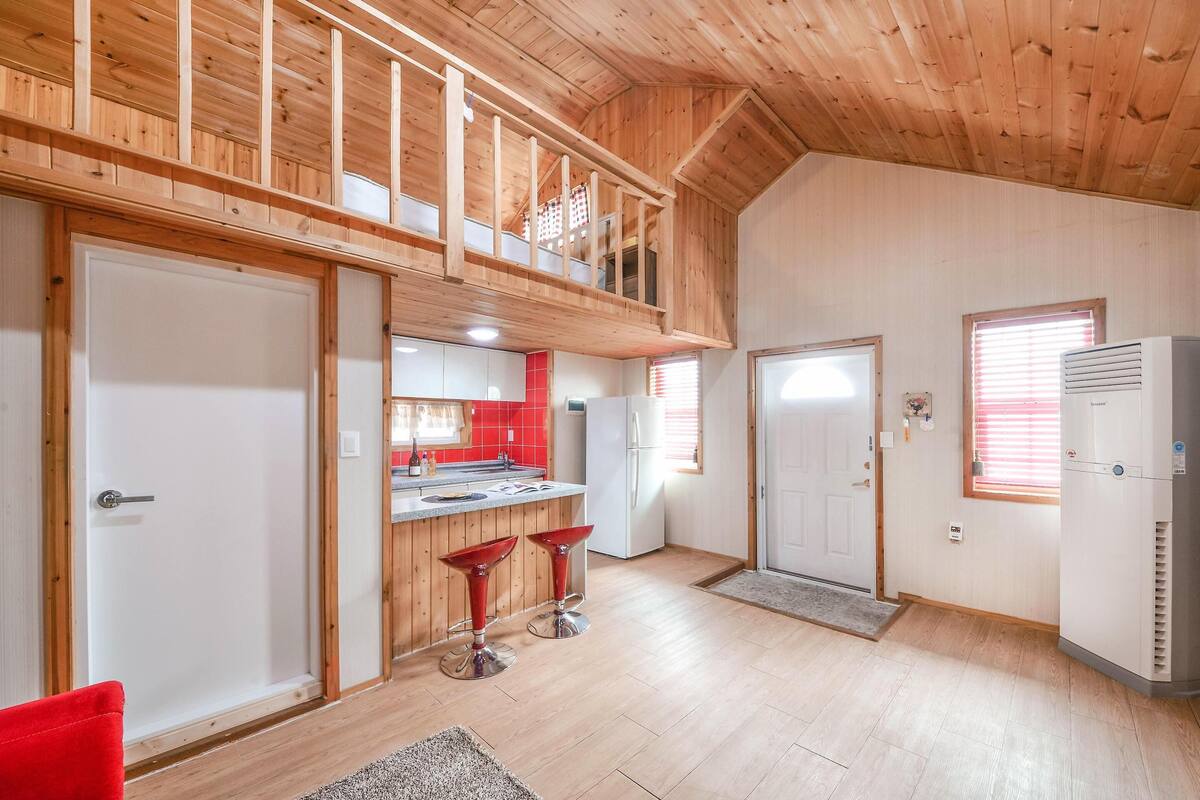 Una cocina amplia con techo de madera, un comedor con taburetes rojos y un pequeño balcón.