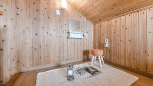 Une pièce aux murs lambrissés, avec un radiateur blanc, un petit tabouret, une lanterne en verre et un magazine posé sur un tapis.