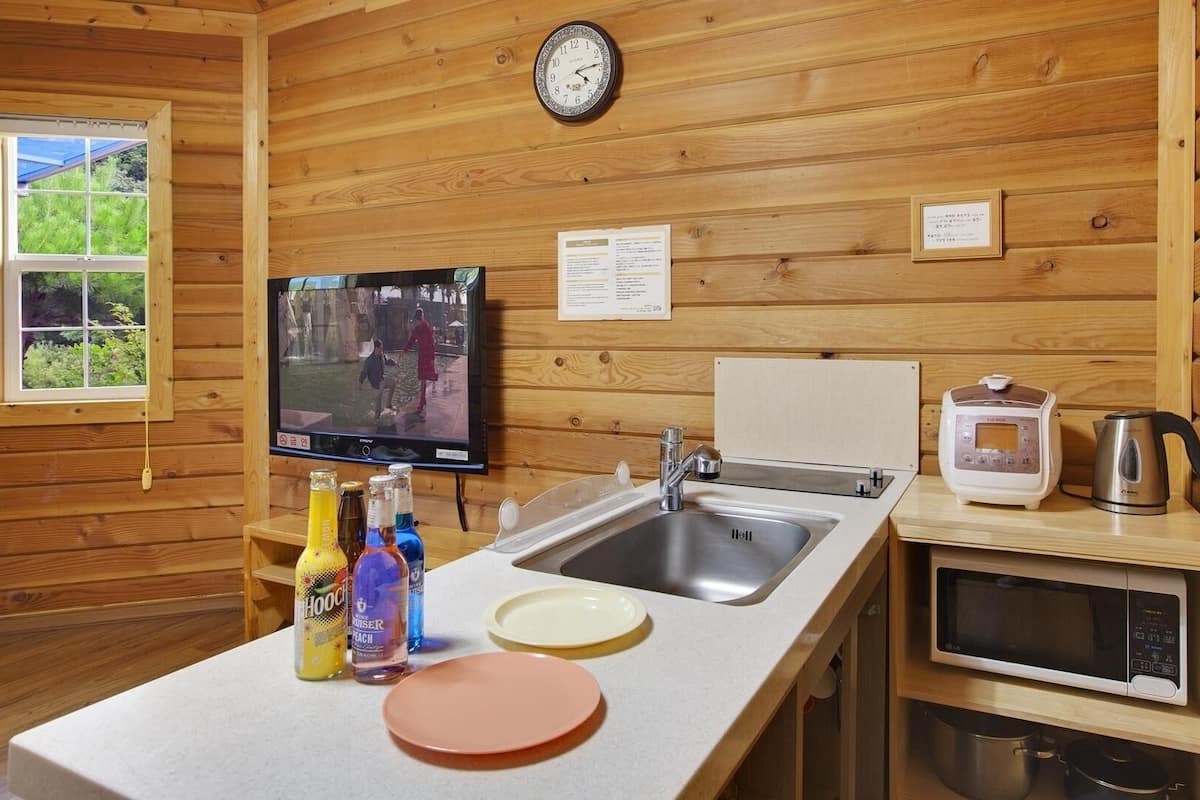 A wooden cabin interior with a kitchen area, including a sink, stove, and a television mounted on the wall.