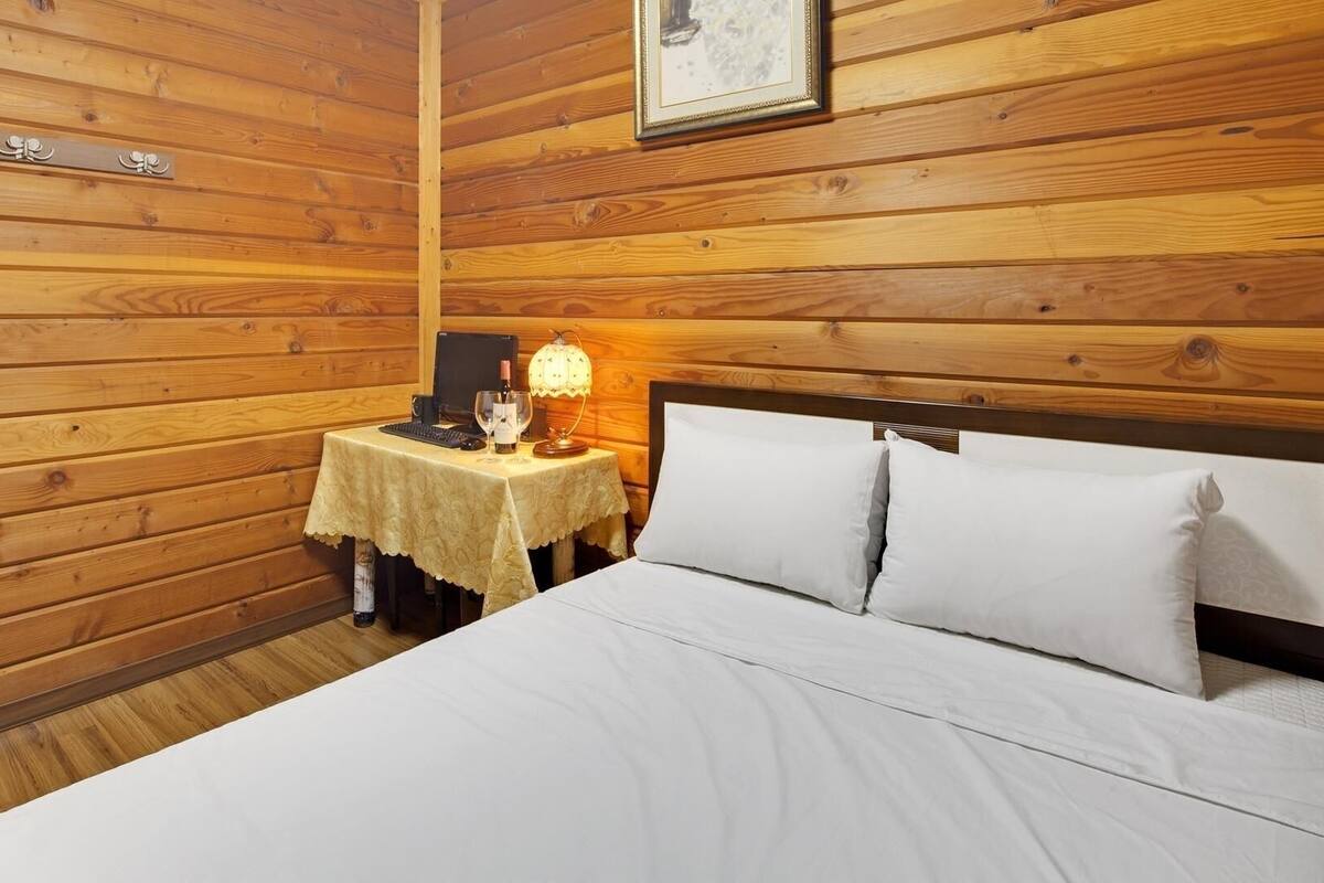 A wooden-paneled room with a bed, a small table with a lamp, and a framed picture on the wall.