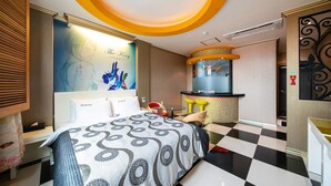 A hotel room with a bed, a desk, a chair, a small table, and a mirror. - Yeosu King Pension Tel (Yeosu)