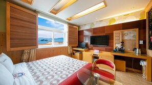 A hotel room with a bed, a desk with a computer, a TV, and a view of the sea. - Yeosu King Pension Tel (Yeosu)