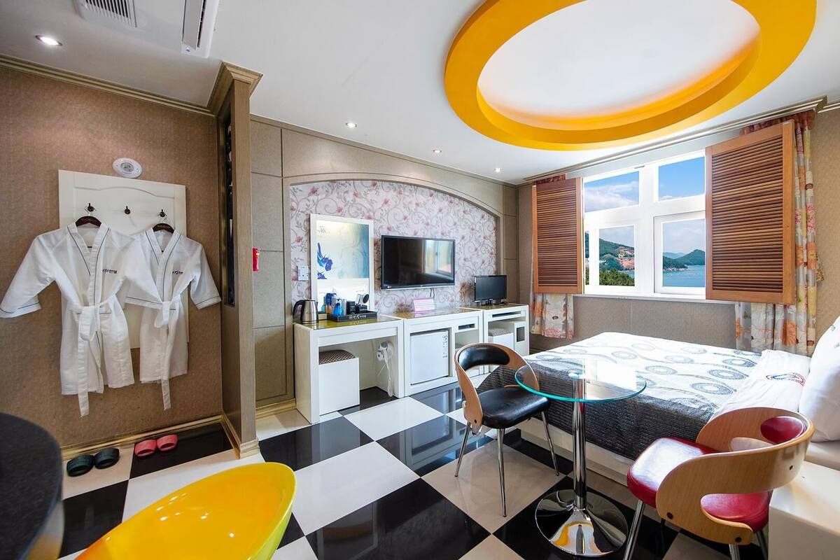 A hotel room with a bed, a desk with a TV, a chair, a table, and a window with a view.