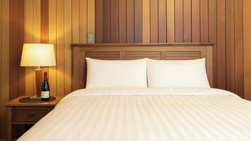A hotel room with a wooden headboard, a bed with white linens, a bedside table with a lamp, and a bottle of wine.