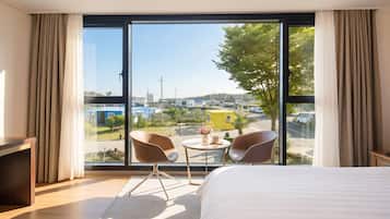 A hotel room with a large window, a bed, two chairs, and a small table.