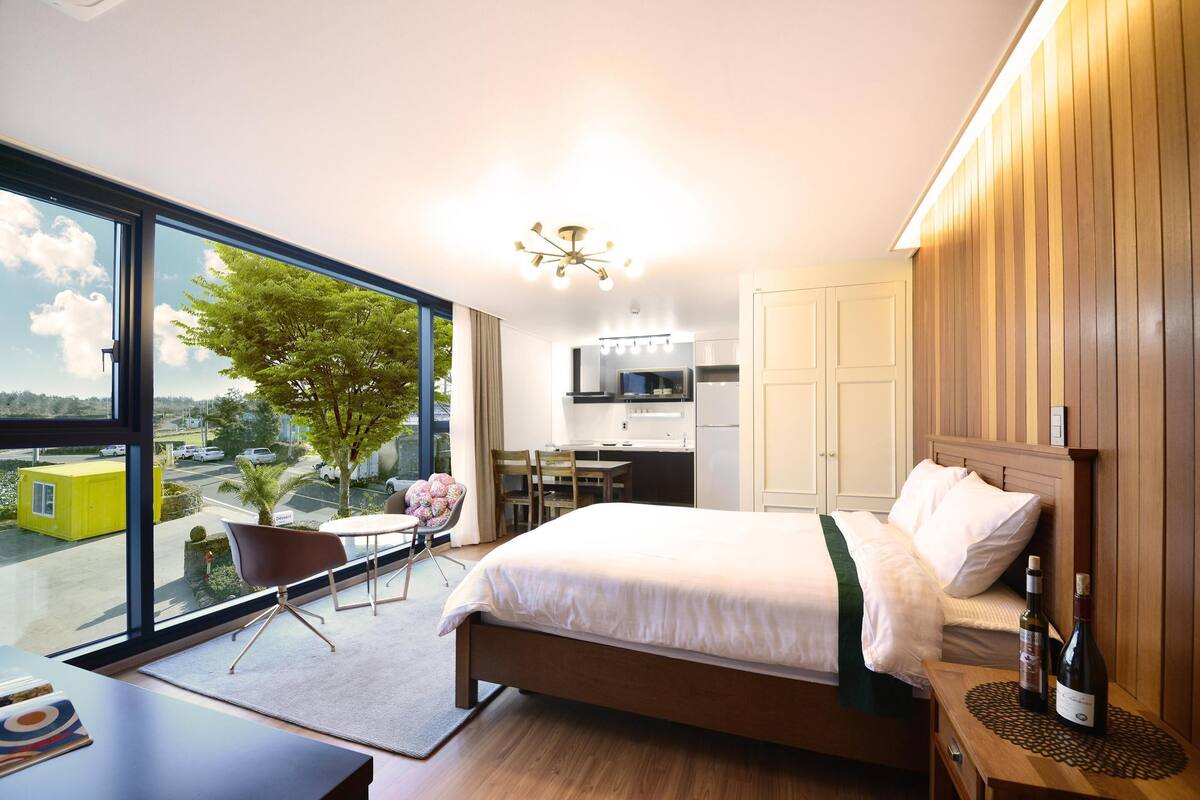 Ein modernes Hotelzimmer mit großem Fenster, einem Bett, einem Schreibtisch und einem Sessel.