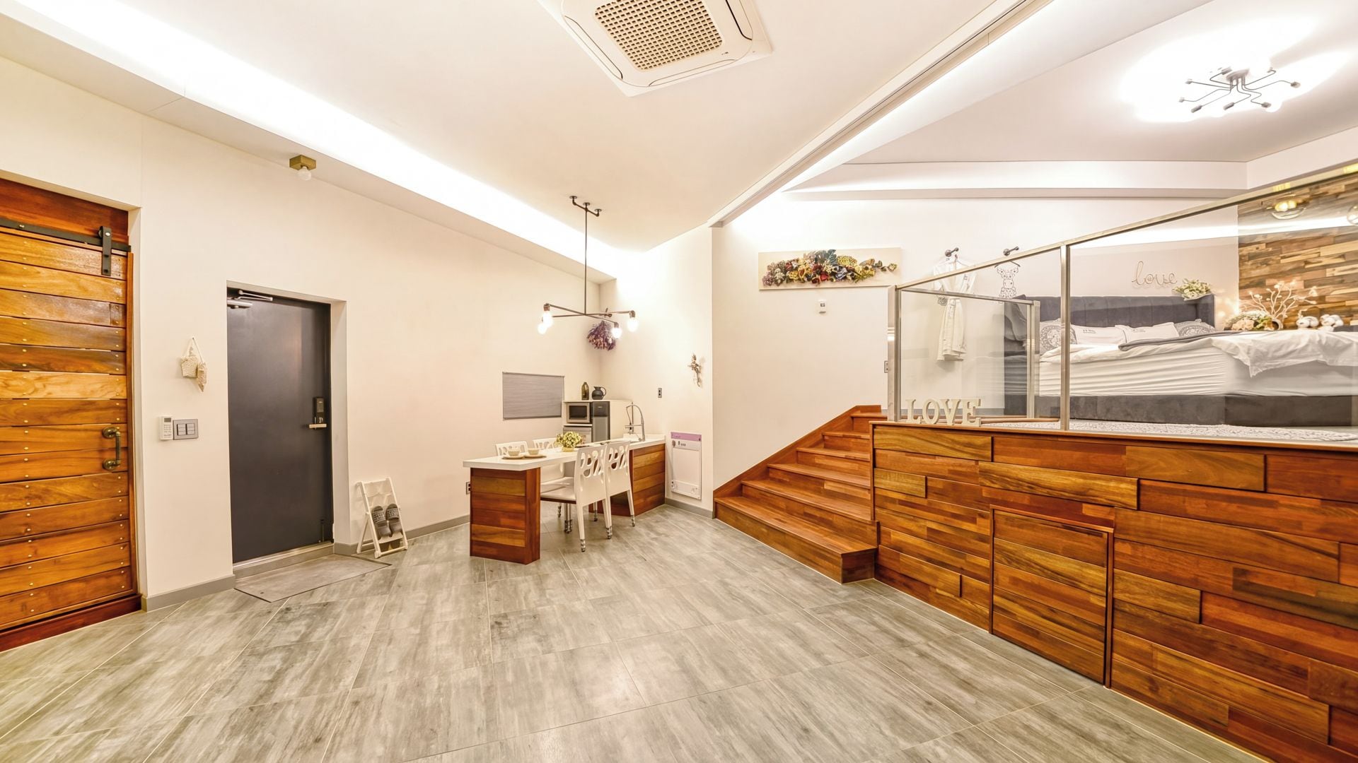 Un interior moderno con suelo de madera, una zona de cocina, un comedor y un espejo grande que refleja la habitación.
