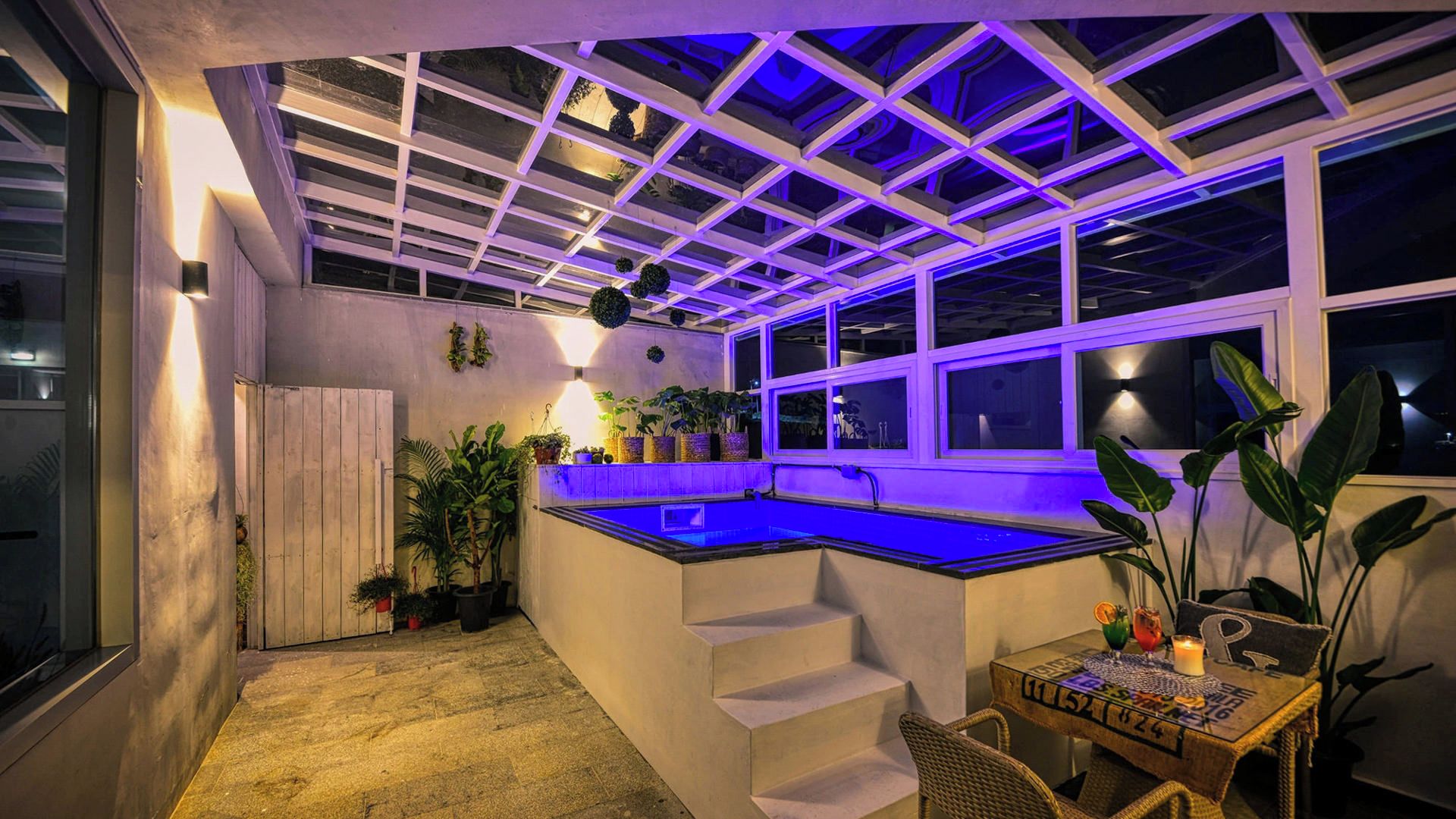 Ein überdachter Außenbereich mit Schwimmbecken, Treppen zu einem fensterartigen Bereich und Topfpflanzen.