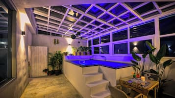 Un espace extérieur abrité avec une piscine, des marches menant à un espace vitré et des plantes en pot.