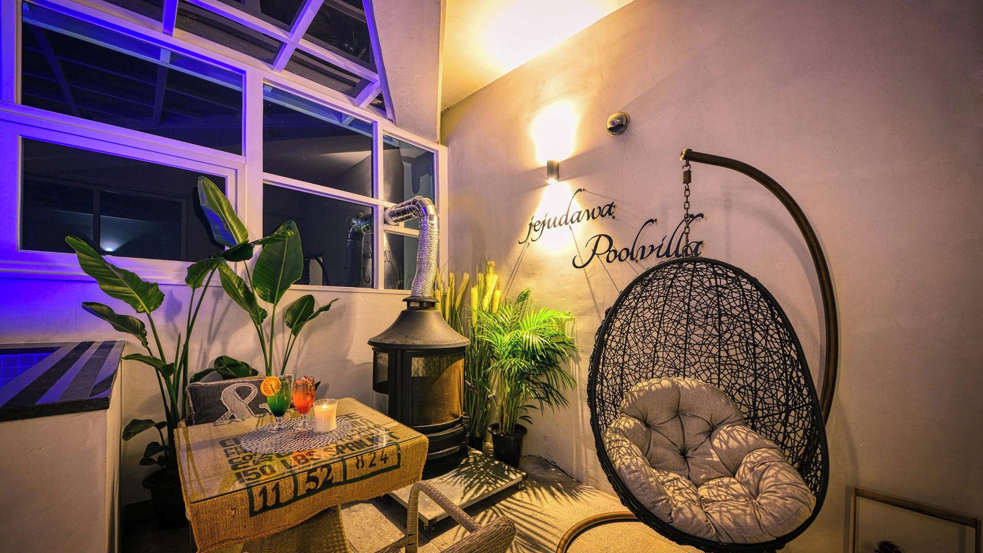Une pièce chaleureuse avec un fauteuil suspendu, une table avec une bougie et un luminaire fixé au mur.