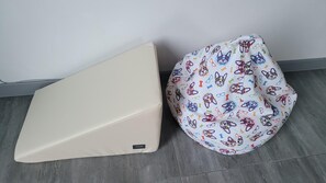 Un sofá color beige y un sillón de peluche de colores, frente a una pared con suelo de baldosas.