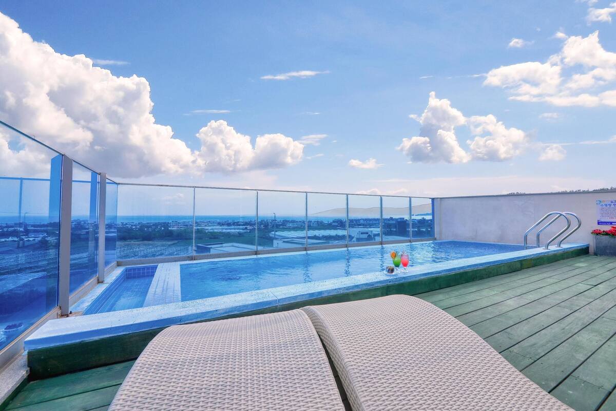 Ein Pool auf dem Dach mit unendlichem Ausblick auf die Stadt, einer Glasumlaufung und Liegestühlen.