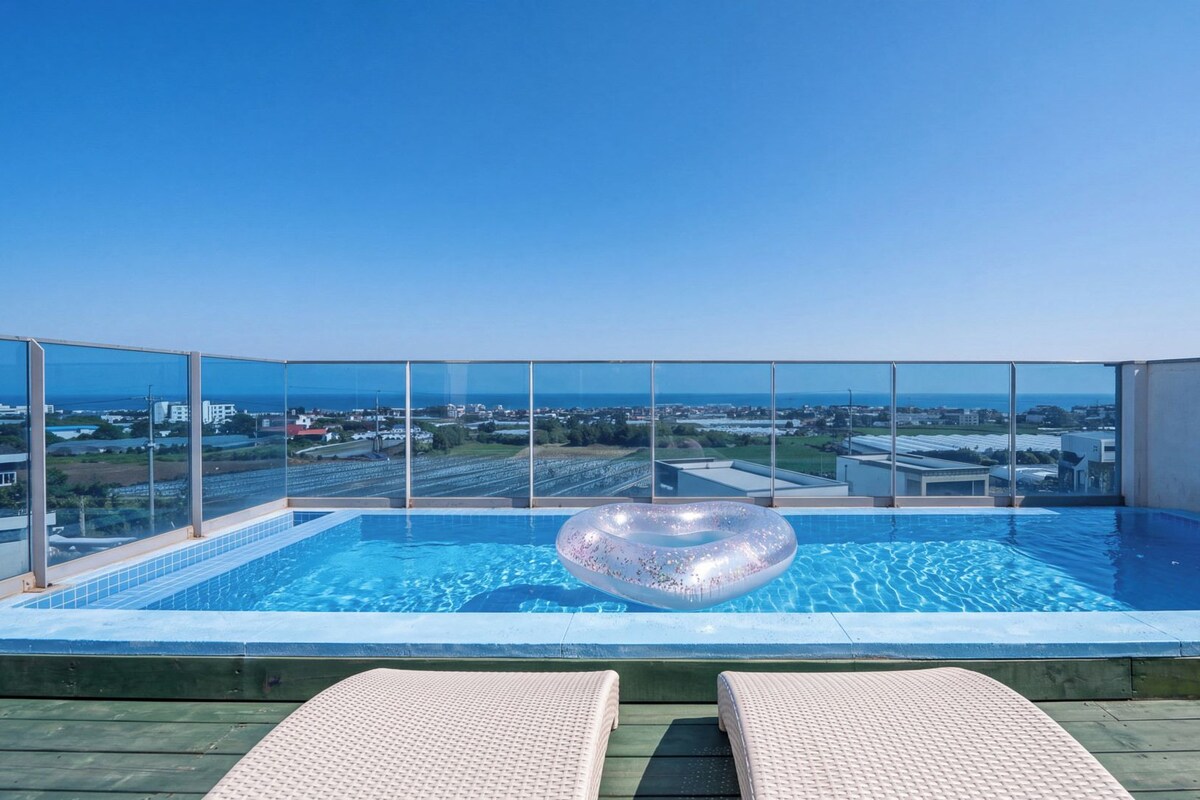 Una piscina infinita en la azotea con barandilla de vidrio, sillones de descanso y una vista despejada del paisaje urbano.