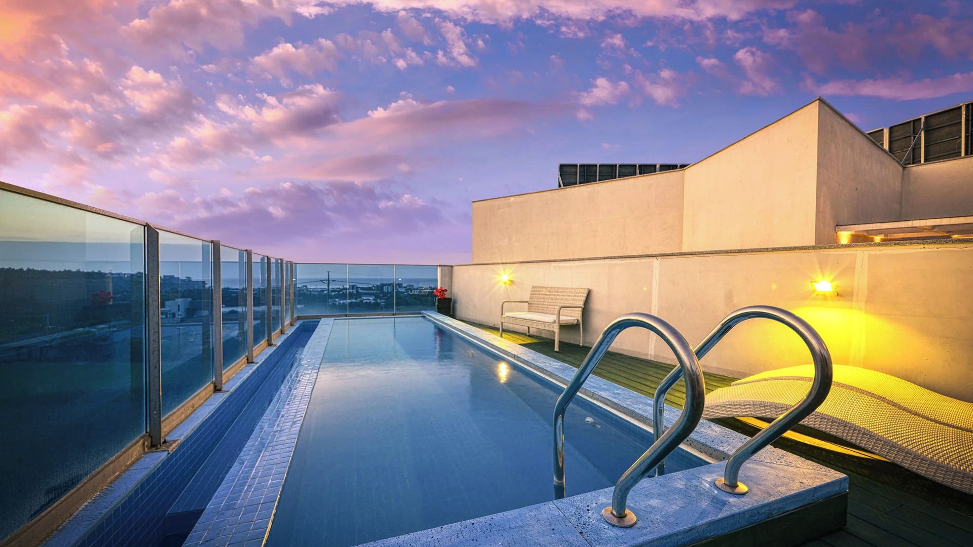 Ein Dachpool mit unendlicher Optik, Glasgeländern, einer Sitzbank und Blick auf die Stadtlandschaft.