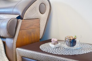 Una butaca de cuero, un panel de madera y una taza de vidrio con una flor sobre una mesa con un mantel de encaje.
