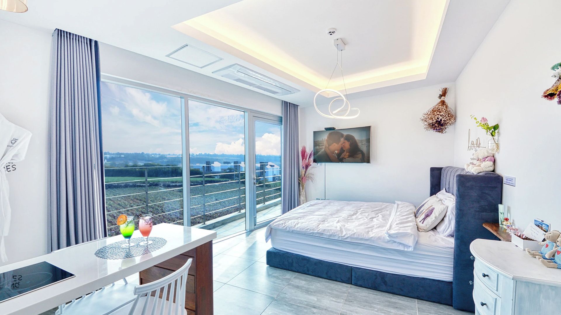 Ein modernes Hotelzimmer mit Balkon, einem Bett, einem Schreibtisch und einem Fernseher.