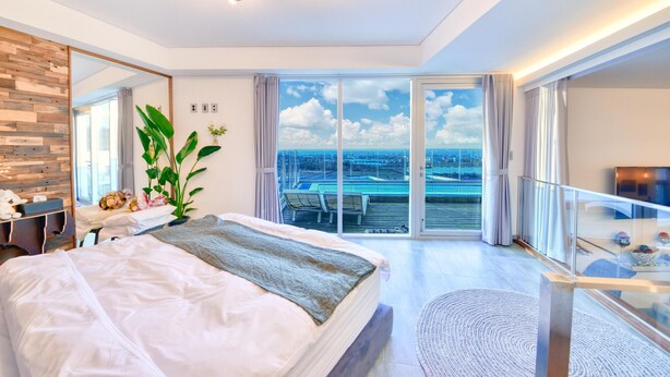 Una camera d'albergo moderna con un letto grande, una scrivania, uno specchio e un balcone con vista sulla città.