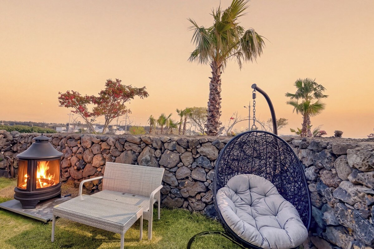 Un patio con muro de piedra, una chimenea, una silla de mimbre y una hamaca colgante.
