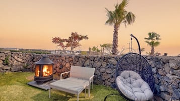 Eine Terrasse mit Steinmauer, Feuerstelle, Korbsessel und Hängesessel.