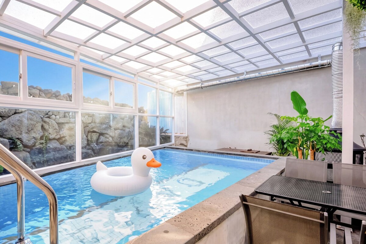 Una piscina interior con un flotador de pato, pared de piedra de fondo y techo de cristal.