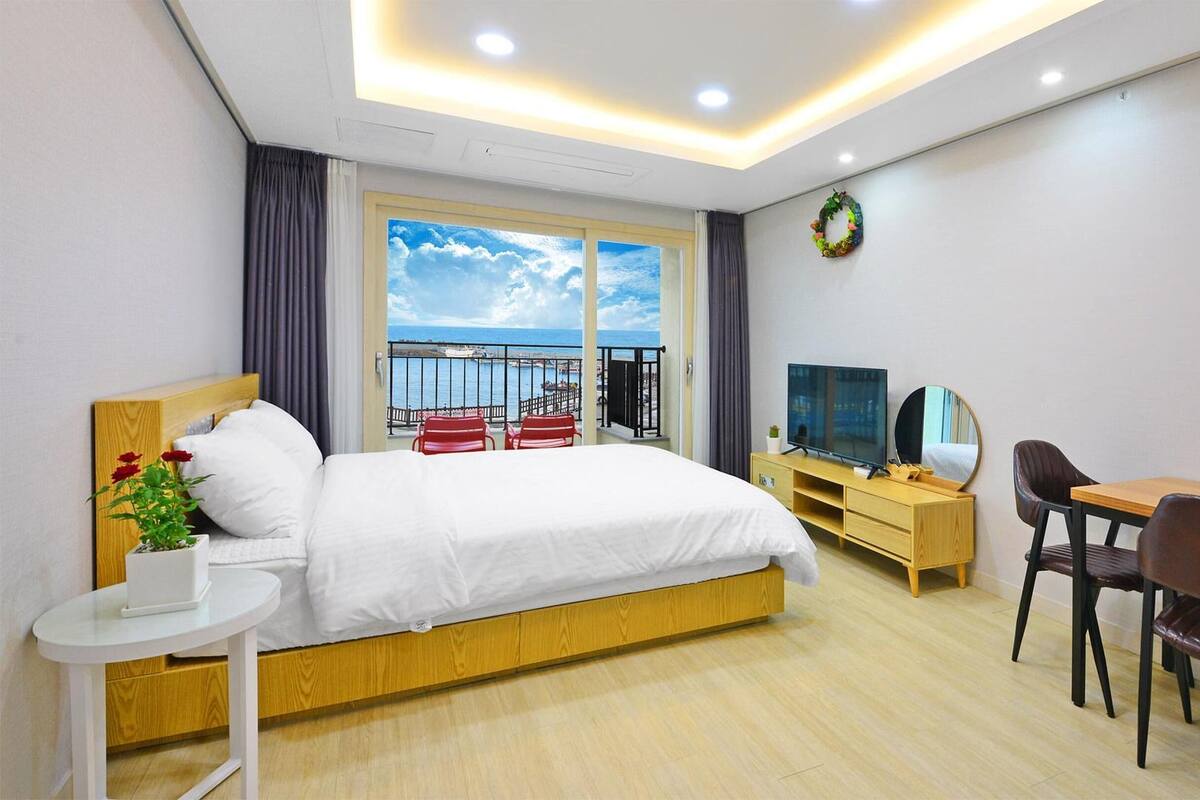 Habitación de hotel con cama, televisión, escritorio y silla. Tiene un balcón con vista al mar.