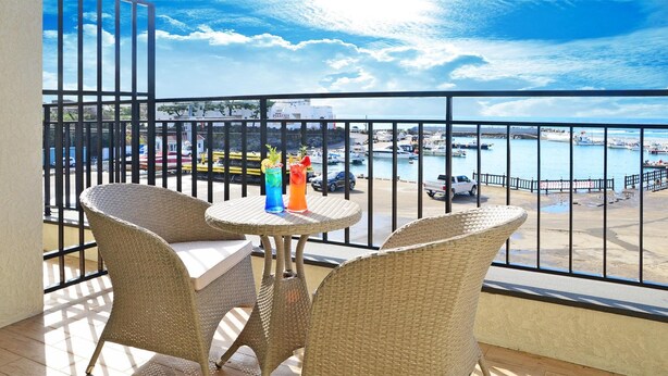 A balcony with wicker chairs and a small table, overlooking a marina with boats and a white building labeled "PIZZERIA". - Seogwipo Daepyeong Olleh Pension (Seogwipo)