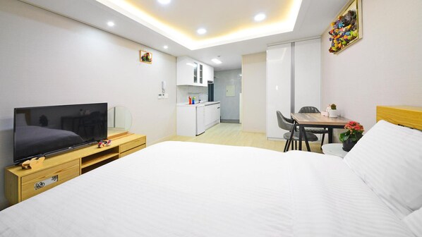 A hotel room with a bed, a TV, a desk with a chair, a small kitchen area, and a bathroom. - Seogwipo Daepyeong Olleh Pension (Seogwipo)