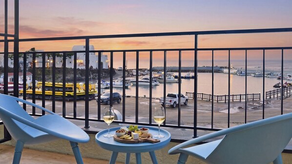 A balcony with two chairs, a small table with a cheese platter and two glasses of wine, overlooking a marina with boats and a sunset. - Seogwipo Daepyeong Olleh Pension (Seogwipo)
