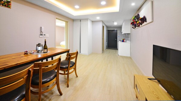 A modern hotel room with a wooden dining table, two chairs, a TV, and a small kitchenette. - Seogwipo Daepyeong Olleh Pension (Seogwipo)