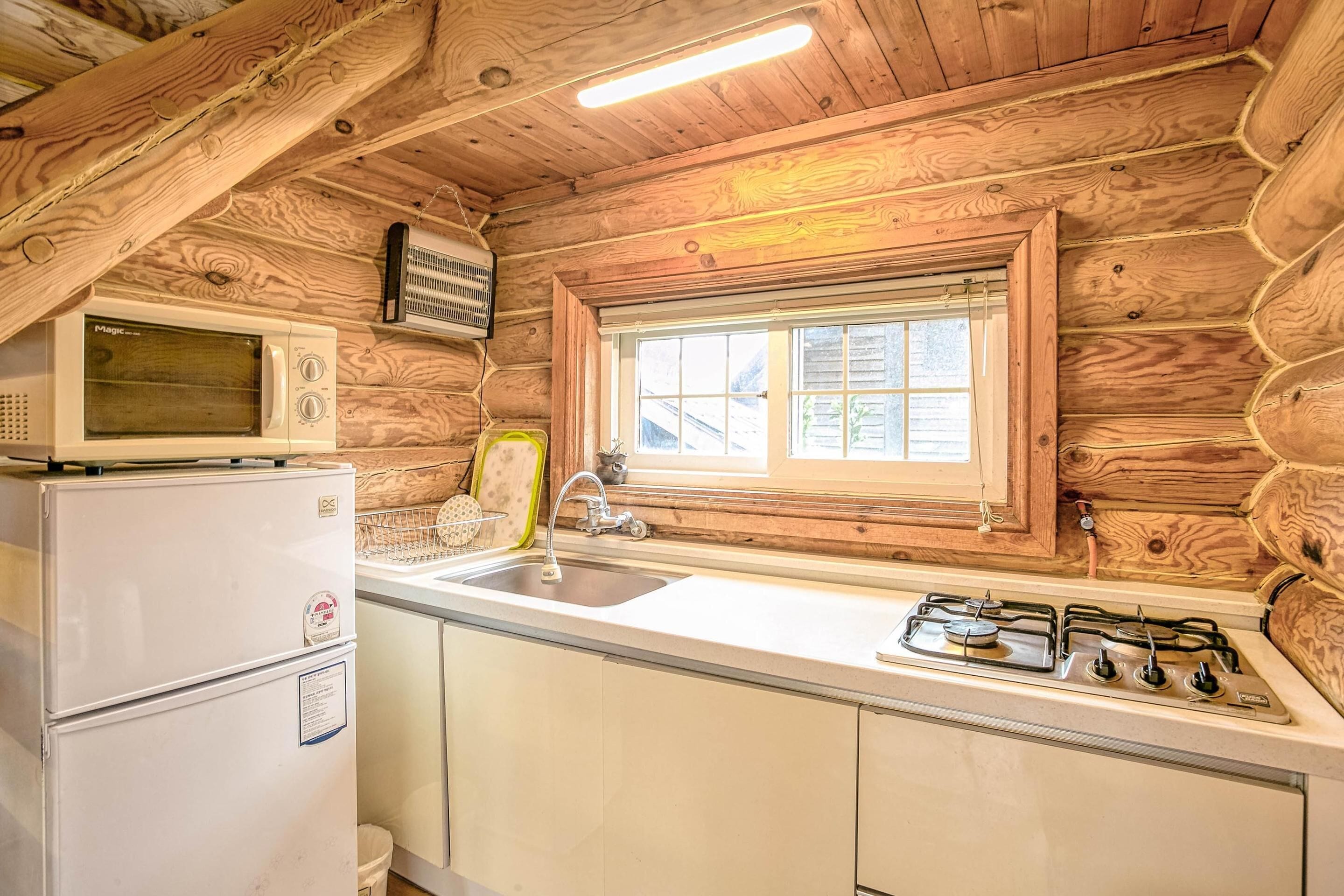 A log cabin kitchen with a refrigerator, microwave, sink, and gas stove.